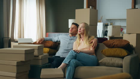 Young-couple-sitting-couch-inspecting-living-room-after-moving-at-new-house.