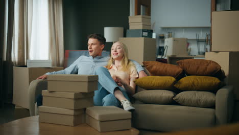 Couple-sitting-new-sofa-excited-about-moving-house.-Man-hugging-blond-woman.