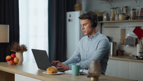 Student-Lernt-Online-Am-Laptop-In-Der-Küche-Mit-Kopfhörern.-Mann-Hört-Webinar