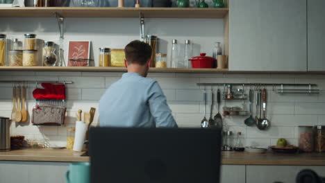 Man-dancing-kitchen-preparing-breakfast.-Guy-answering-video-call-at-laptop.