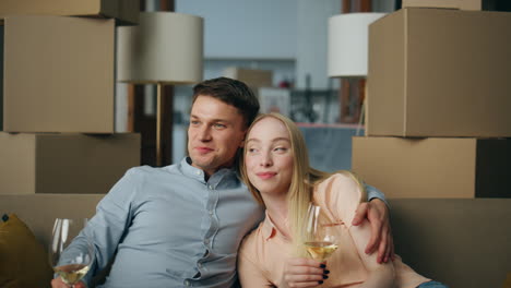 Couple-celebrating-buying-house-sitting-in-living-room-with-wine-goblets-closeup