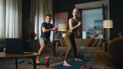 Man-workouting-woman-in-room-watching-video-lesson.-Fit-family-couple-training.