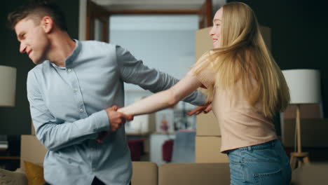 Funny-couple-dancing-moving-in-new-apartment-full-of-packed-carton-boxes-closeup