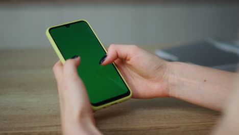 Woman-holding-greenscreen-smartphone-scrolling-touchscreen-at-home-close-up.