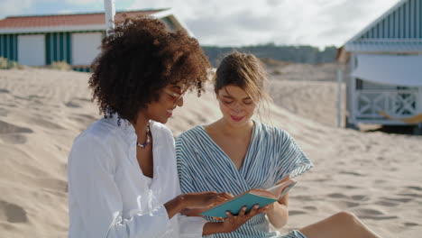 Two-girls-reading-book-on-summer-beach-picnic.-Happy-lesbian-couple-talking