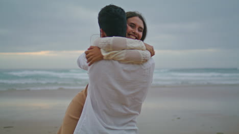 Engaged-couple-embracing-at-ocean-sunset-beach-closeup.-Boyfriend-swirling-bride