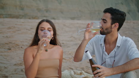 Smiling-couple-clinking-wine-glasses-beach-picnic.-Family-celebrating-honeymoon