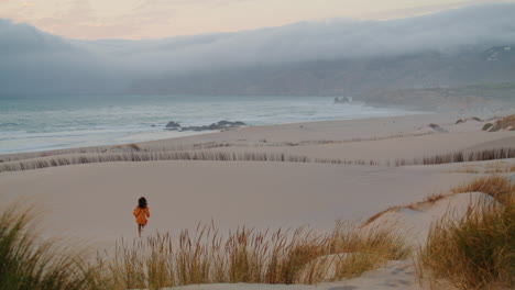 Girl-running-sand-seashore-gloomy-evening-in-distance.-Woman-jogging-empty-beach