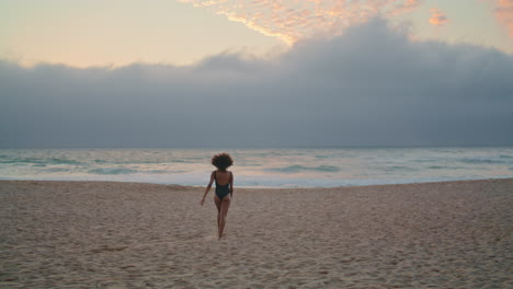 Relaxed-woman-enjoy-seashore-walking-on-sand-near-ocean-waves-back-view.