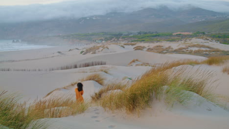 Girl-running-down-sand-dunes-at-overcast-evening.-Woman-jogging-on-seashore.