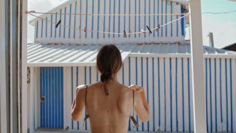 Topless-girl-taking-bikini-bra-off-in-house-vertically.-Slim-woman-hang-swimsuit
