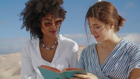 Laughing-women-reading-book-on-beach-closeup.-Love-partners-enjoying-summer