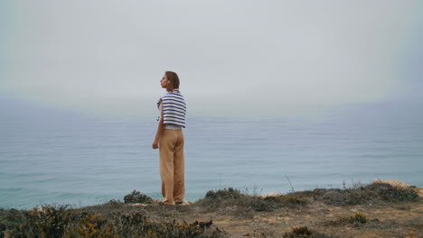 Depressed-person-looking-ocean-on-cliff-edge-vertical-shot.-Pensive-girl-resting