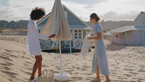 Girls-resting-beach-picnic-at-coastline-houses.-Happy-friends-preparing-spot