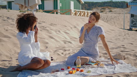 Lgbt-couple-taking-photos-on-sandy-seashore.-Two-happy-girls-having-picnic-fun