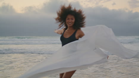 Woman-running-beach-fabric-in-front-gray-cloudy-sky.-Girl-waving-satin-pareo.