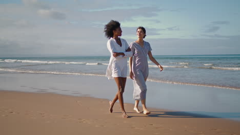 Happy-women-enjoying-ocean-walk.-Smiling-lesbian-couple-resting-sandy-beach