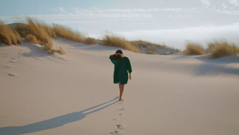 Woman-walking-desert-dunes-in-black-dress.-Girl-stepping-sand-making-footmarks.