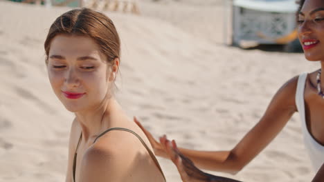 Friends-applying-suntan-cream-on-beach-closeup.-Happy-girlfriends-resting-summer