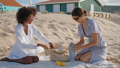 Lgbt-couple-enjoying-picnic-at-beach-houses-sunny-summer-day.-Happy-girls-rest