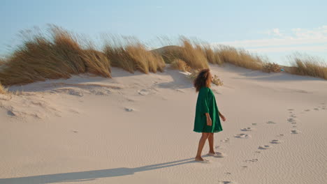 Girl-jogging-down-sand-hill-leaving-footprints-on-desert.-Brunette-enjoy-holiday
