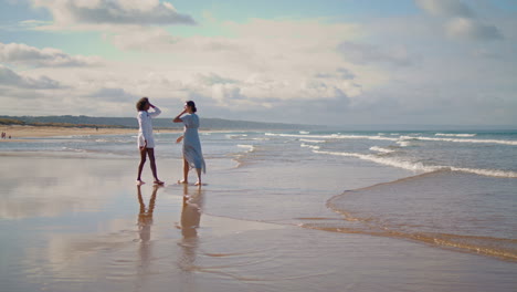 Vertical-view-lesbian-couple-walking-beach-in-summer.-Best-friends-resting-ocean