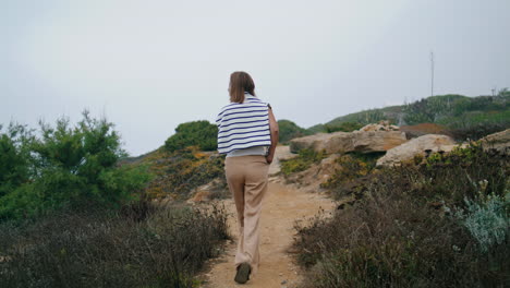 Girl-walking-rocky-path-rear-vertical-view.-Serene-tourist-enjoy-trekking-summer