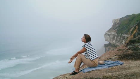 Thinking-girl-relaxing-ocean-cliff-vertical.-Serene-woman-enjoy-seashore-waves