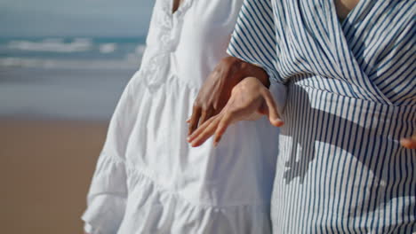 Closeup-couple-hands-walking-ocean-coast-in-sunlight.-Girlfriends-enjoying-date