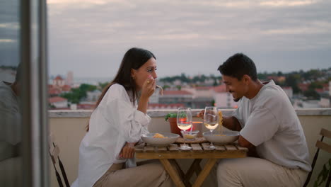 Love-pair-enjoying-food-at-sunset-city-view-balcony.-Couple-celebrating-vertical