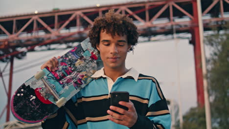 Contemporary-skateboarder-texting-phone-closeup.-Curly-man-carrying-longboard