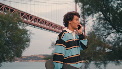 Friendly-teenager-speaking-smartphone-at-embankment.-Guy-talking-mobile-vertical