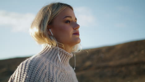 Walking-girl-wearing-headphones-nature-background.-Blonde-lady-listening-music