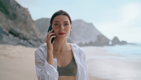 Happy-girl-speaking-smartphone-standing-gloomy-beach-close-up-vertical-view.