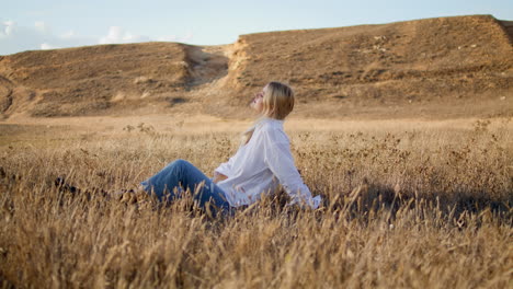 Contemplative-girl-sitting-field-alone.-Vertically-blonde-woman-putting-spikelet