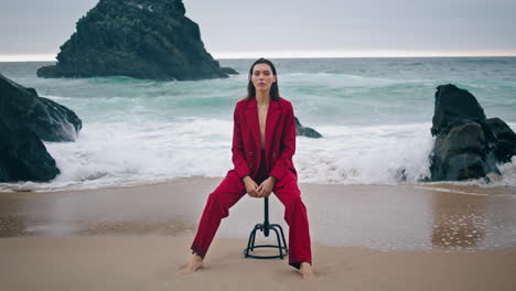Model-posing-camera-coast-in-red-suit.-Woman-sitting-chair-at-ocean-vertical