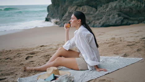 Girl-eating-apple-beach-picnic-sitting-at-blanket.-Woman-enjoy-fruit-vertically