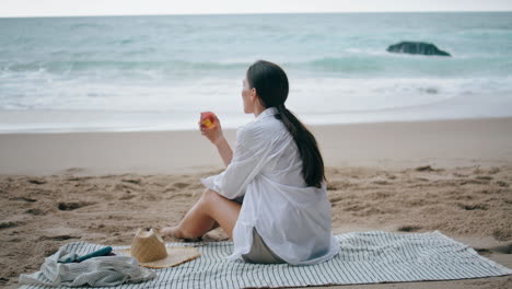 Mujer-Relajante-Picnic-En-La-Playa-Sentada-En-Una-Manta.-Niña-Disfrutando-De-Frutas-En-La-Orilla-Del-Mar