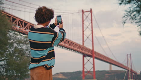 Young-tourist-photographing-bridge-evening-closeup.-Guy-with-smartphone-vertical
