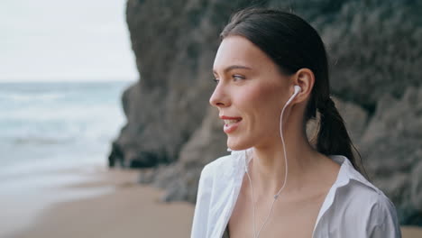 Woman-answering-phone-headphones-standing-beach-in-front-sandy-hill-close-up.