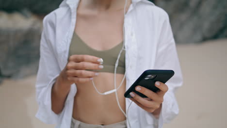 Young-girl-putting-headphones-on-beach-close-up.-Woman-turning-on-mobile-app.