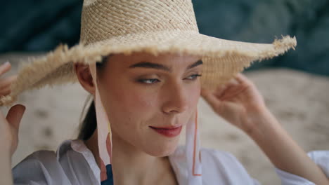 Woman-putting-straw-hat-sitting-sand-beach-closeup.-Portrait-young-girl-on-shore