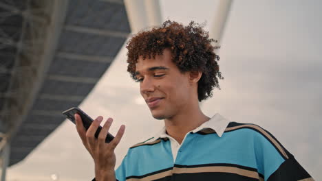 Modern-guy-listening-mobile-voice-message-at-street.-Teen-holding-phone-vertical