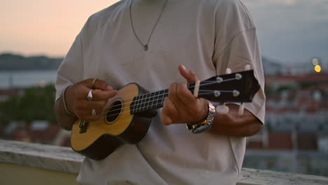 Thoughtful-guy-signing-sunset-terrace-on-weekend.-Man-play-ukulele-on-evening