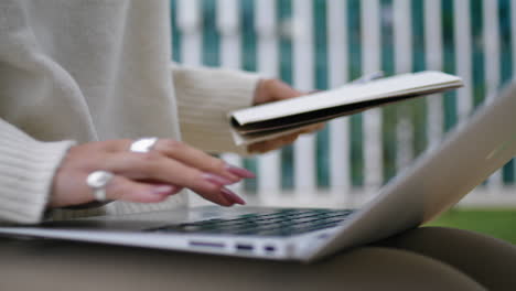 Woman-hands-typing-laptop-outdoors-holding-copybook-closeup.-Freelancer-vertical