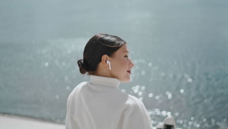 Relaxed-girl-listening-music-in-earbuds-sitting-at-waterfront-closeup-vertically