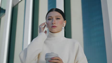 Woman-wearing-wireless-earbuds-in-ears-standing-near-urban-building-close-up.