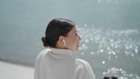 Young-woman-speaking-wireless-earphones-sitting-quay-at-weekend-closeup-vertical