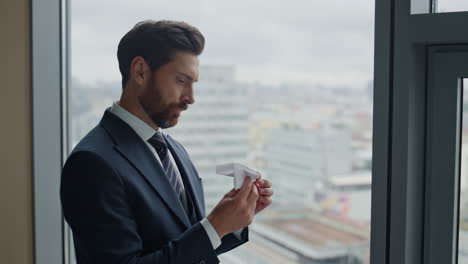 Manager-holding-paper-airplane-standing-at-window-looking-cityscape-close-up.