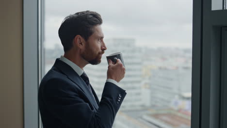 Ceo-manager-enjoy-coffee-break-standing-at-office-window-close-up.-Man-drinking.